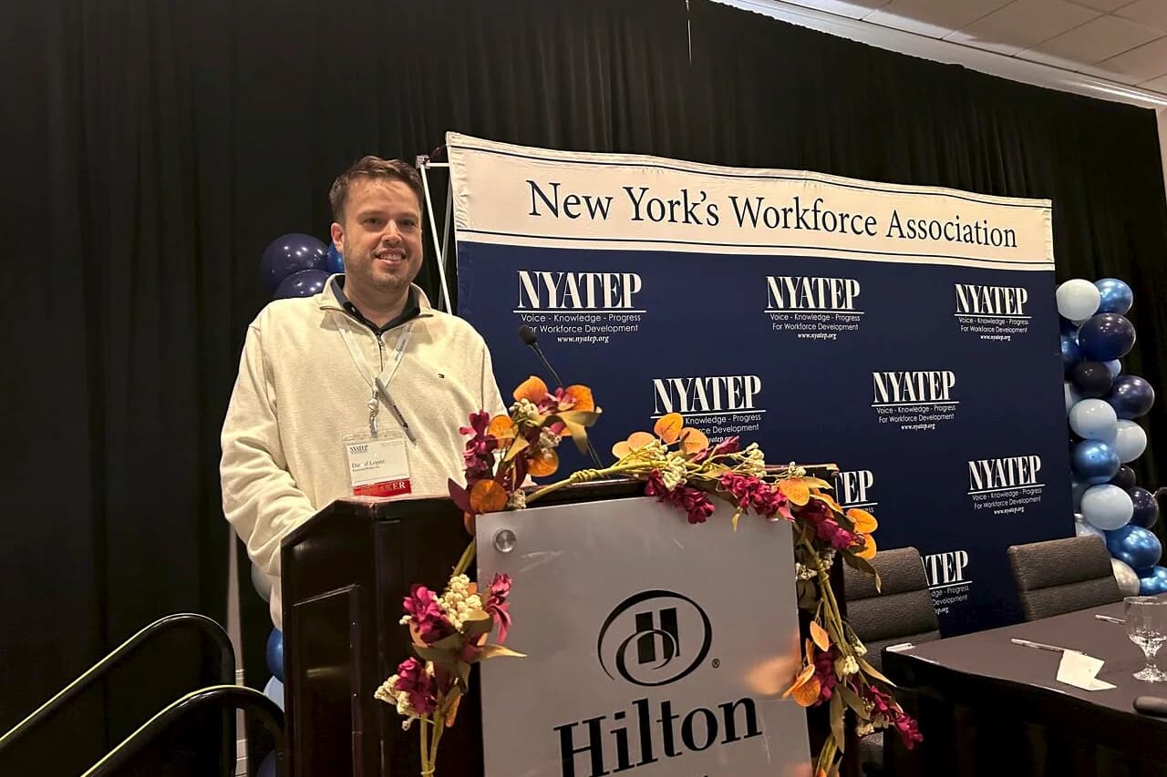 Dan Lopez smiling at a podium, wearing a speaker badge, in front of a NYATEP backdrop that reads New York’s Workforce Association.